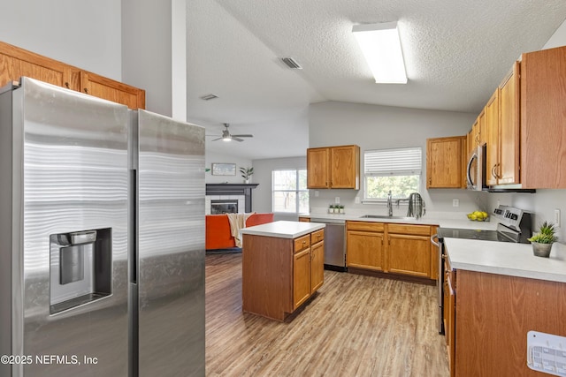 kitchen with ceiling fan, a center island, lofted ceiling, a tiled fireplace, and appliances with stainless steel finishes