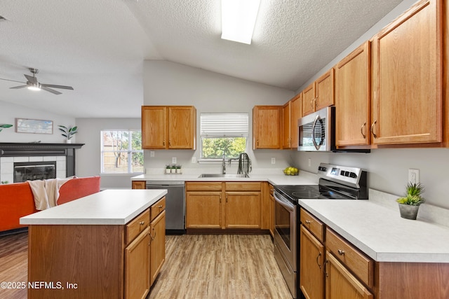 kitchen with a tile fireplace, sink, vaulted ceiling, a textured ceiling, and appliances with stainless steel finishes