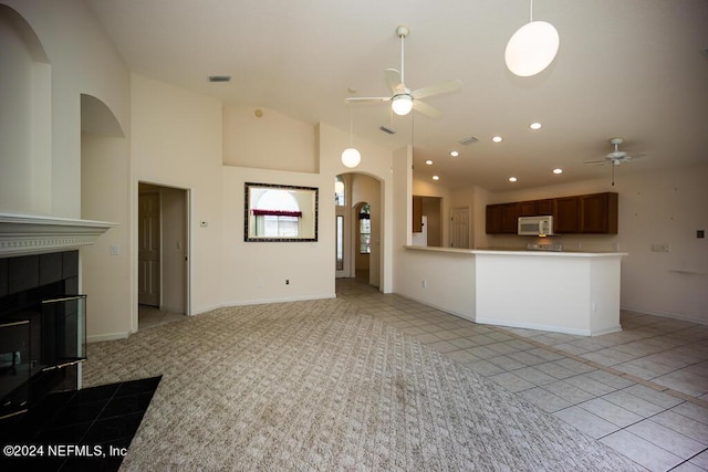 unfurnished living room with a tiled fireplace, light tile patterned floors, high vaulted ceiling, and ceiling fan