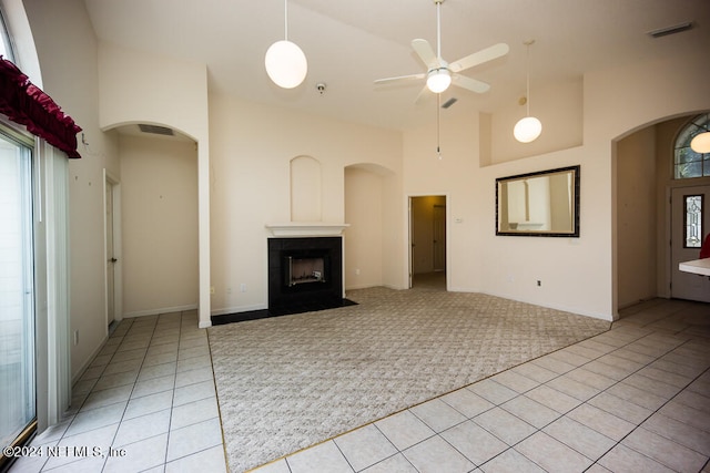 unfurnished living room with ceiling fan, light carpet, a tiled fireplace, and high vaulted ceiling