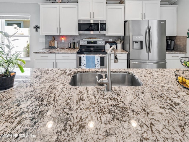 kitchen featuring light stone counters, backsplash, sink, white cabinets, and appliances with stainless steel finishes