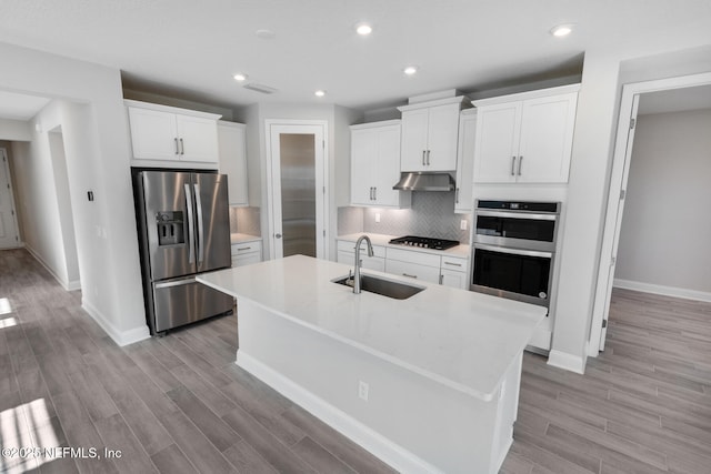 kitchen featuring a kitchen island with sink, under cabinet range hood, a sink, light countertops, and appliances with stainless steel finishes