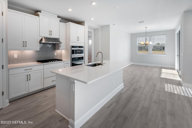 kitchen featuring light countertops, a sink, a kitchen island with sink, and white cabinets