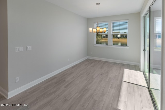 unfurnished dining area with light wood-type flooring, baseboards, and an inviting chandelier