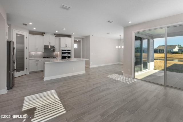 kitchen featuring a center island with sink, visible vents, freestanding refrigerator, white cabinets, and under cabinet range hood