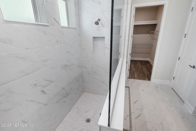 bathroom with marble finish floor, baseboards, a walk in closet, and tiled shower