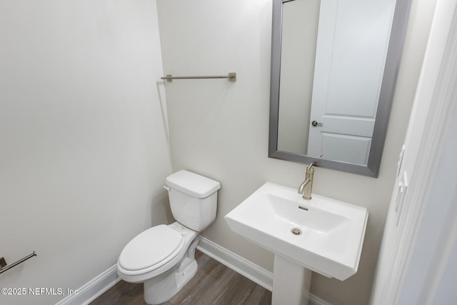 half bath featuring toilet, baseboards, a sink, and wood finished floors