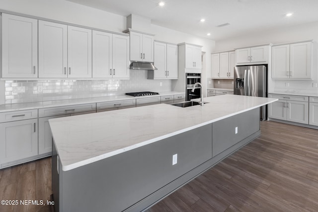 kitchen with dark wood-style floors, a kitchen island with sink, stainless steel appliances, under cabinet range hood, and a sink