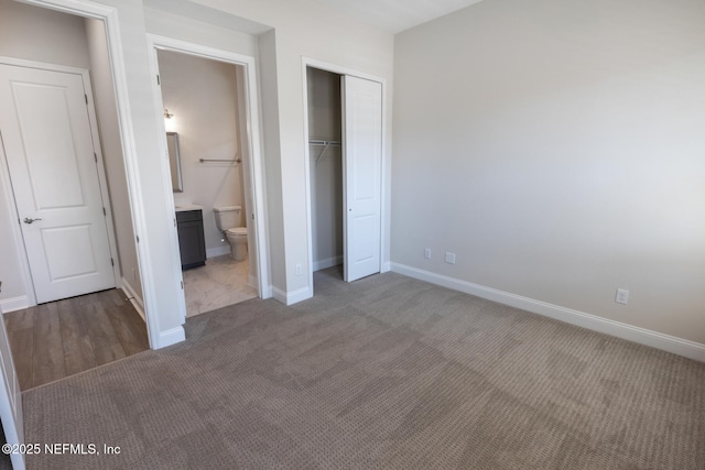 unfurnished bedroom featuring a closet, light colored carpet, baseboards, and ensuite bathroom