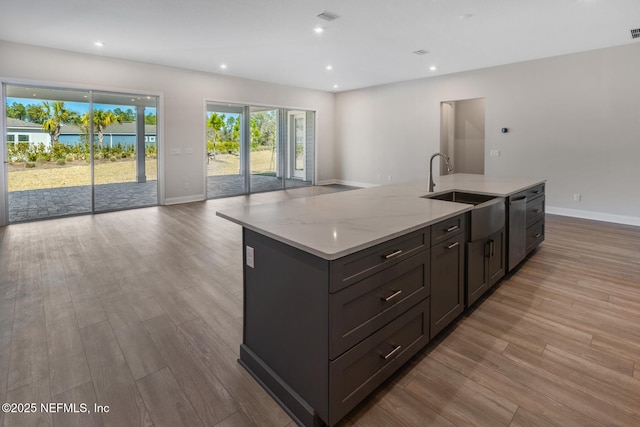 kitchen with open floor plan, a sink, light wood finished floors, and an island with sink