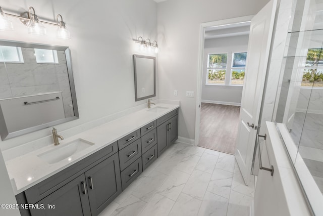 full bath featuring marble finish floor, a sink, a tile shower, and double vanity