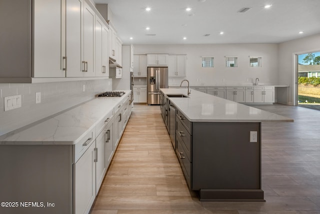 kitchen featuring a large island, light stone countertops, stainless steel appliances, white cabinetry, and a sink