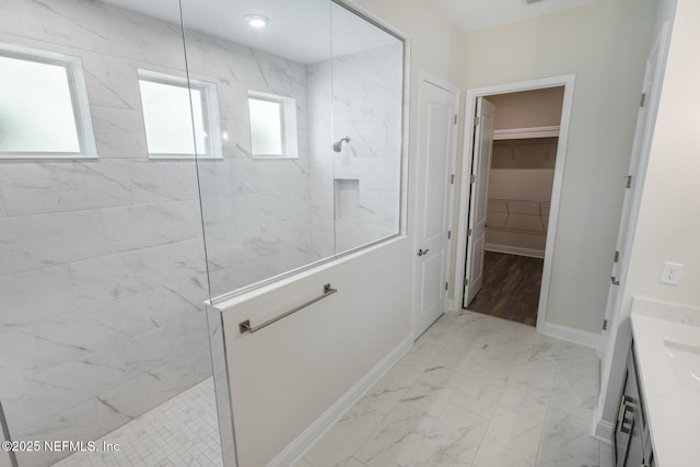 bathroom featuring a walk in shower, vanity, baseboards, marble finish floor, and a spacious closet