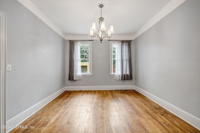 empty room with ornamental molding, a notable chandelier, and light wood-type flooring