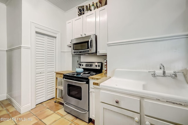 kitchen featuring crown molding, white cabinetry, appliances with stainless steel finishes, and light tile floors