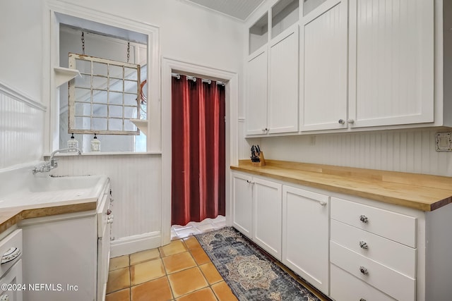 kitchen featuring white cabinetry, light tile flooring, sink, butcher block counters, and ornamental molding