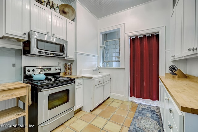 kitchen with ornamental molding, white cabinets, light tile floors, and stainless steel appliances