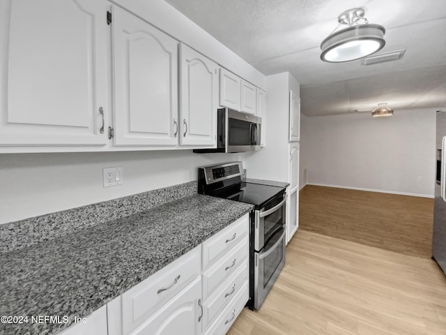 kitchen featuring white cabinetry, light wood-type flooring, dark stone counters, stainless steel appliances, and a textured ceiling