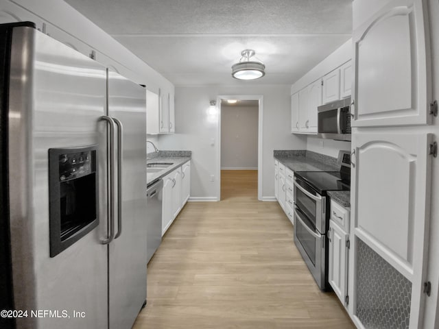 kitchen featuring appliances with stainless steel finishes, white cabinetry, sink, dark stone counters, and light hardwood / wood-style floors