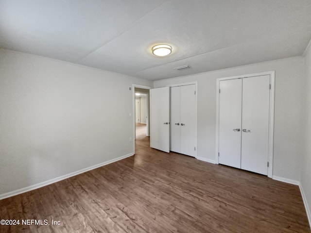 unfurnished bedroom featuring dark hardwood / wood-style flooring and multiple closets