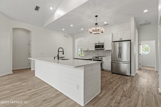 kitchen with a kitchen island with sink, stainless steel appliances, sink, decorative light fixtures, and white cabinetry