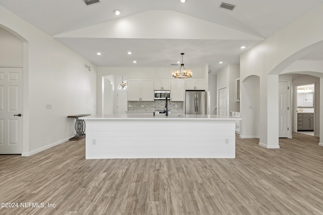 kitchen featuring a large island with sink, appliances with stainless steel finishes, vaulted ceiling, pendant lighting, and light hardwood / wood-style flooring