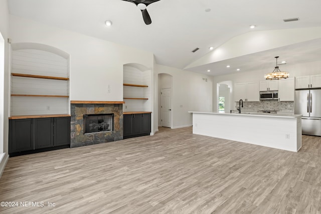 unfurnished living room with lofted ceiling, light hardwood / wood-style flooring, sink, a fireplace, and ceiling fan