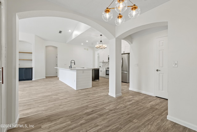 kitchen with hanging light fixtures, white cabinetry, stainless steel appliances, light hardwood / wood-style flooring, and a kitchen island with sink