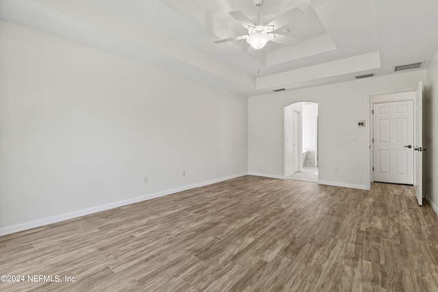 empty room with ceiling fan, a raised ceiling, and light wood-type flooring