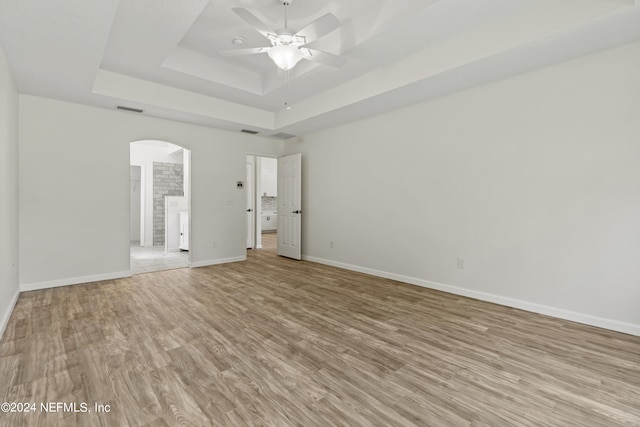 unfurnished room featuring a tray ceiling, light wood-type flooring, and ceiling fan