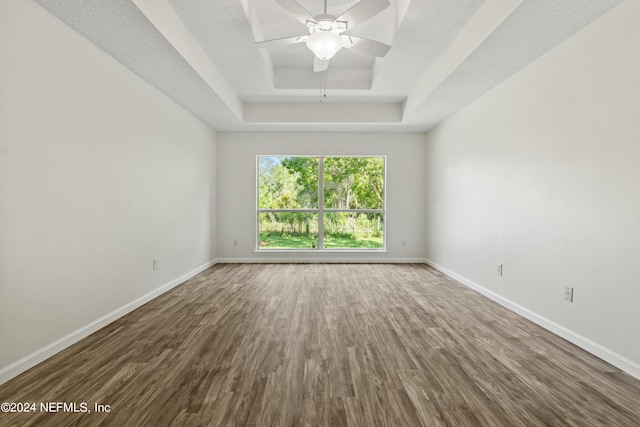 spare room with a textured ceiling, hardwood / wood-style flooring, a tray ceiling, and ceiling fan