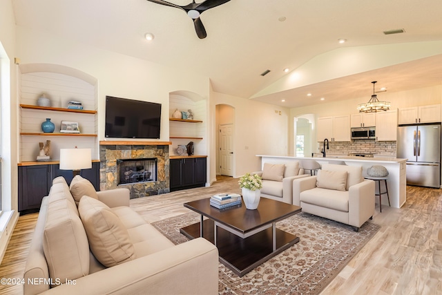 living room featuring lofted ceiling, a fireplace, light wood-type flooring, and ceiling fan with notable chandelier