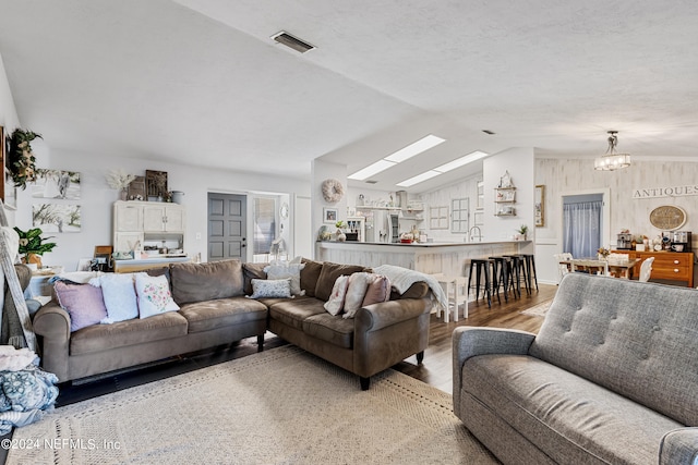 living room with lofted ceiling with skylight, a notable chandelier, wood-type flooring, and sink