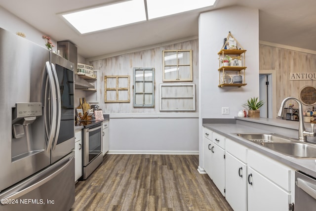 kitchen featuring vaulted ceiling with skylight, wooden walls, appliances with stainless steel finishes, white cabinetry, and sink