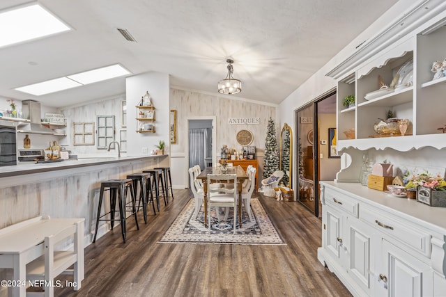 dining area with lofted ceiling with skylight, a chandelier, and dark wood-type flooring