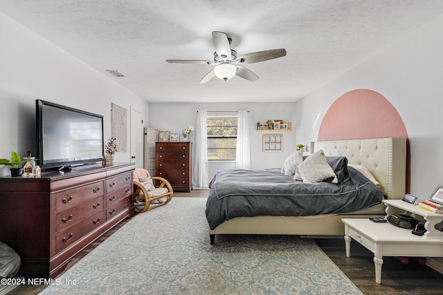 bedroom with a textured ceiling, ceiling fan, and dark hardwood / wood-style flooring