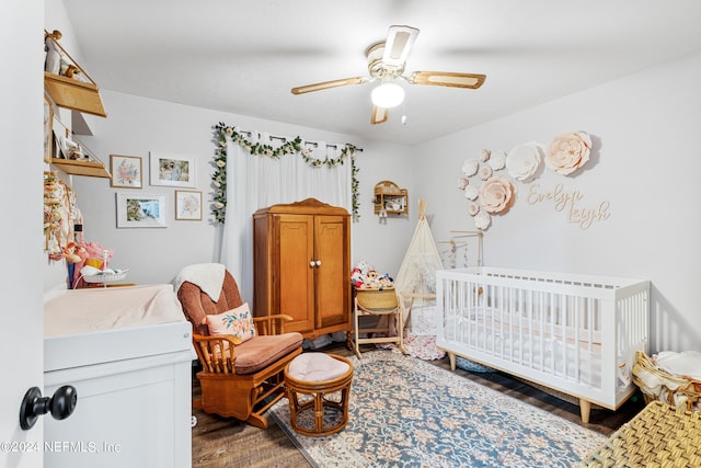 bedroom with dark hardwood / wood-style floors, a nursery area, and ceiling fan