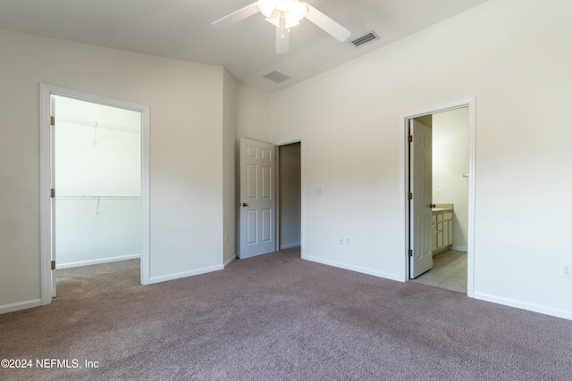 unfurnished bedroom with light carpet, ensuite bath, ceiling fan, a spacious closet, and a closet