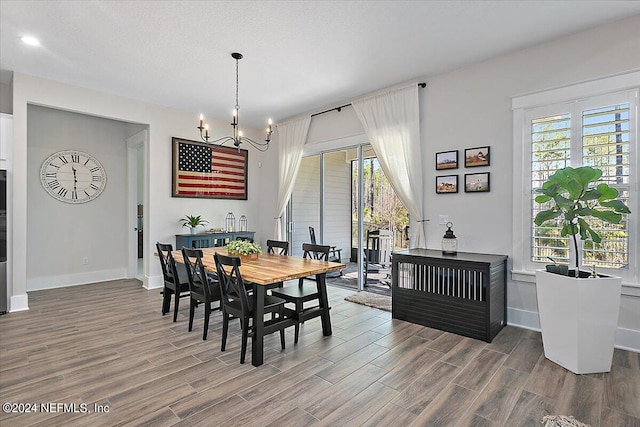 dining room featuring a healthy amount of sunlight, wood-type flooring, and an inviting chandelier