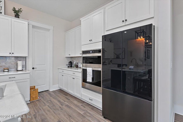 kitchen with backsplash, double oven, white cabinetry, and hardwood / wood-style flooring