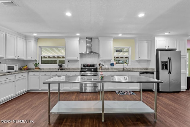 kitchen featuring appliances with stainless steel finishes, dark wood-type flooring, wall chimney exhaust hood, and white cabinetry