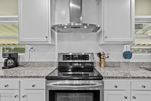 kitchen with wall chimney range hood, tasteful backsplash, white cabinetry, and stainless steel electric stove