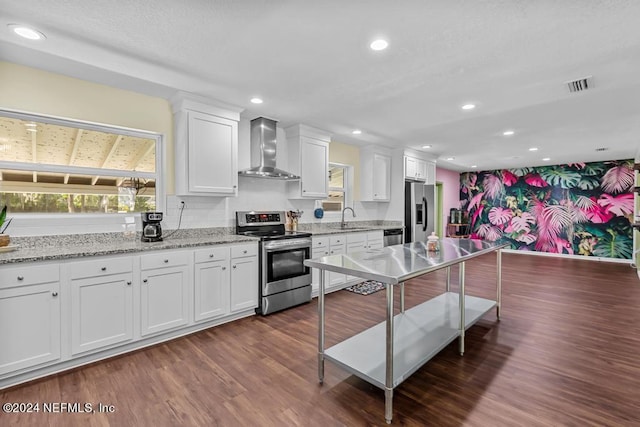 kitchen with dark hardwood / wood-style flooring, white cabinets, appliances with stainless steel finishes, light stone countertops, and wall chimney range hood