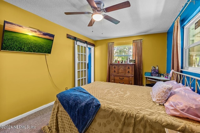 bedroom featuring a barn door, a textured ceiling, carpet flooring, and ceiling fan