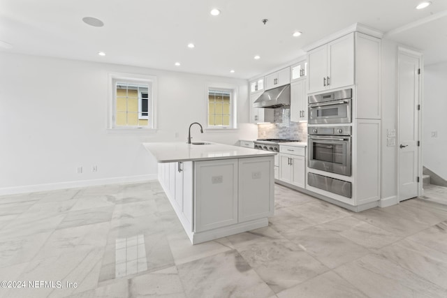 kitchen featuring white cabinetry, backsplash, stainless steel appliances, and a center island with sink