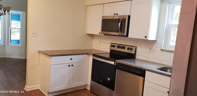 kitchen featuring appliances with stainless steel finishes, white cabinetry, dark stone counters, and backsplash