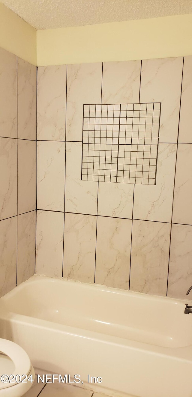 bathroom featuring tiled shower / bath combo, a textured ceiling, and toilet