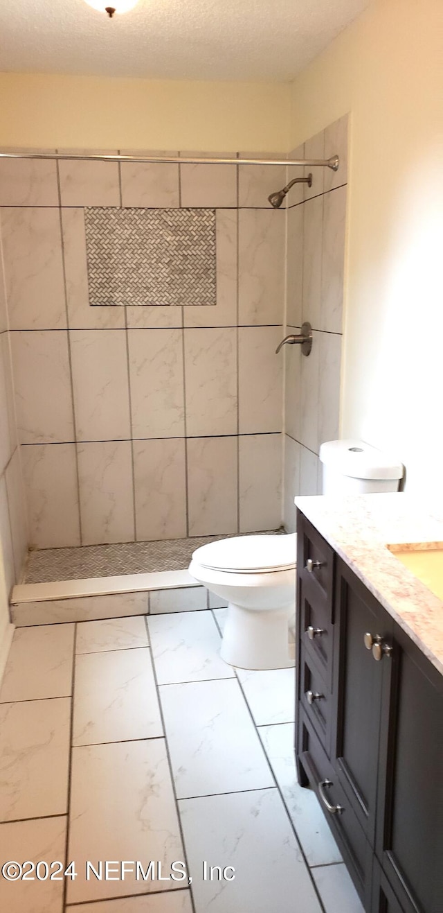 bathroom featuring toilet, a textured ceiling, vanity, tile flooring, and a tile shower