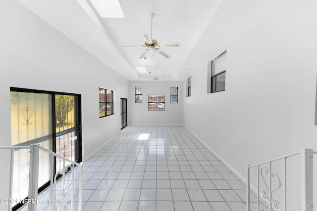 empty room featuring a skylight, ceiling fan, light tile patterned flooring, and a wealth of natural light