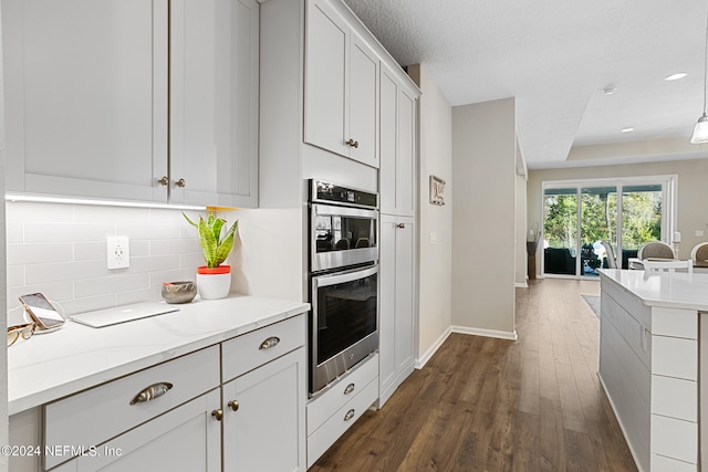 kitchen featuring stainless steel double oven, dark wood-type flooring, white cabinetry, open floor plan, and backsplash